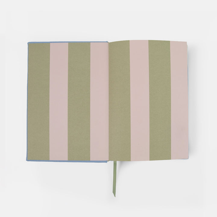 An open notebook with alternating vertical stripes in sage green and dusty pink, featuring a light blue cover edge and a matching green ribbon bookmark, shot against a clean white background.