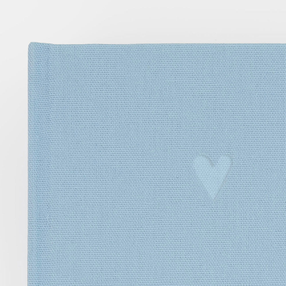 A close-up of a light blue textured fabric with a small tonal embroidered heart on the right side, shown against a plain white background.