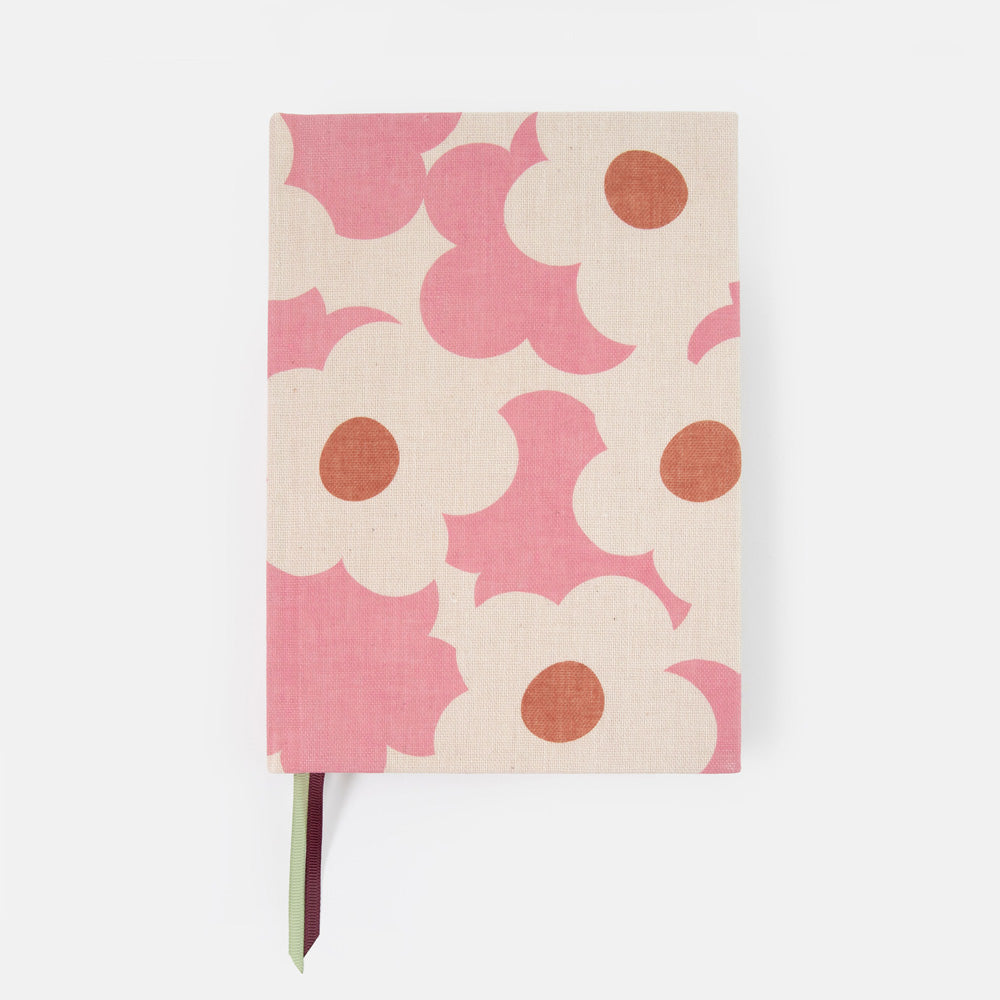 A hardcover notebook with a pink and cream floral pattern, featuring a small green and burgundy ribbon bookmark hanging from the bottom.