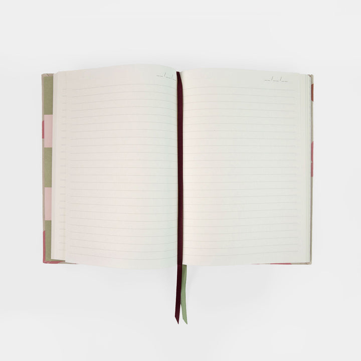 An open lined notebook with cream-colored pages, a dark burgundy ribbon bookmark, and a pastel patterned cover in pink, green, and white, shown against a plain white background.