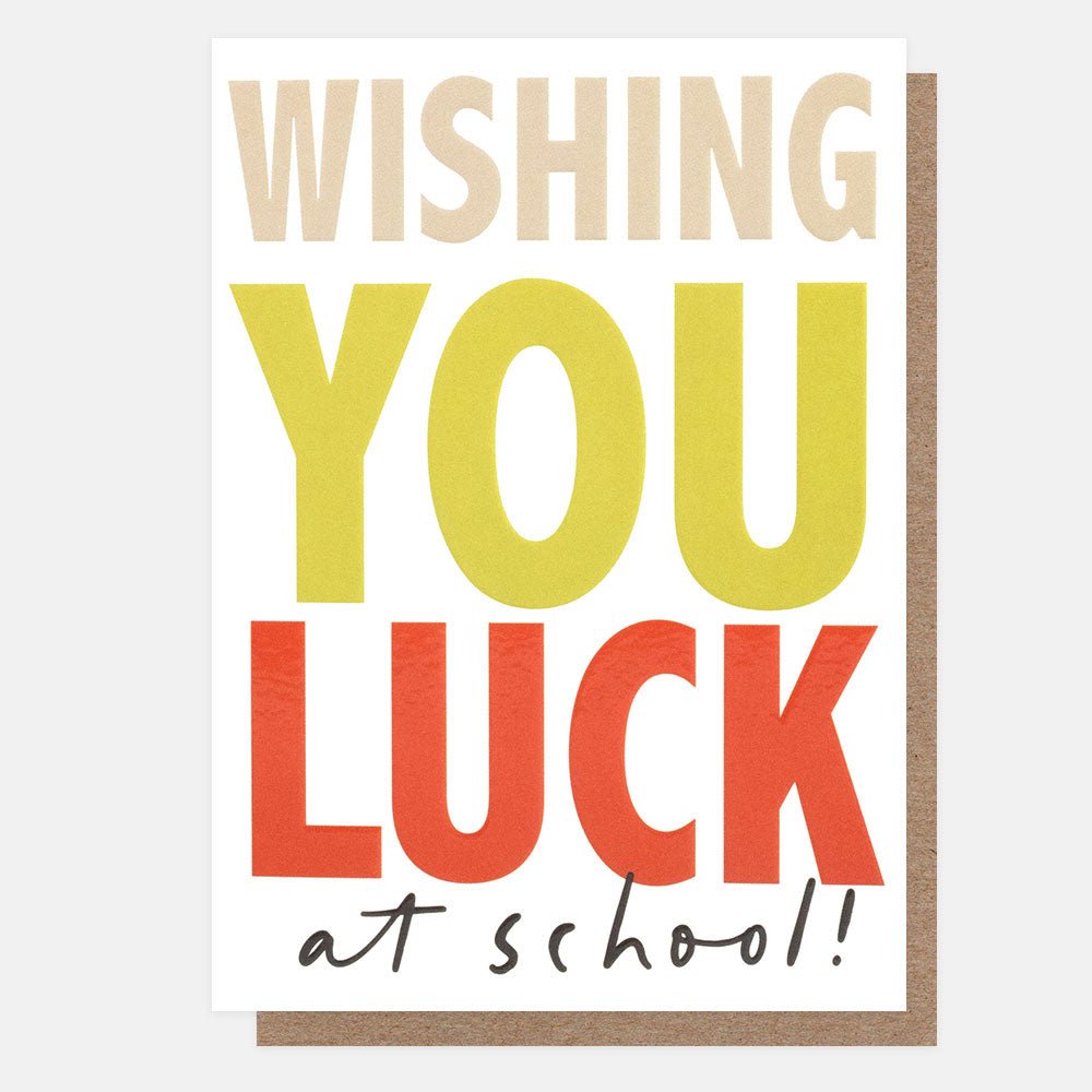 A greeting card with a white front and kraft brown envelope behind it. The card reads “WISHING YOU LUCK at school!” in large colorful letters on a light gray background.