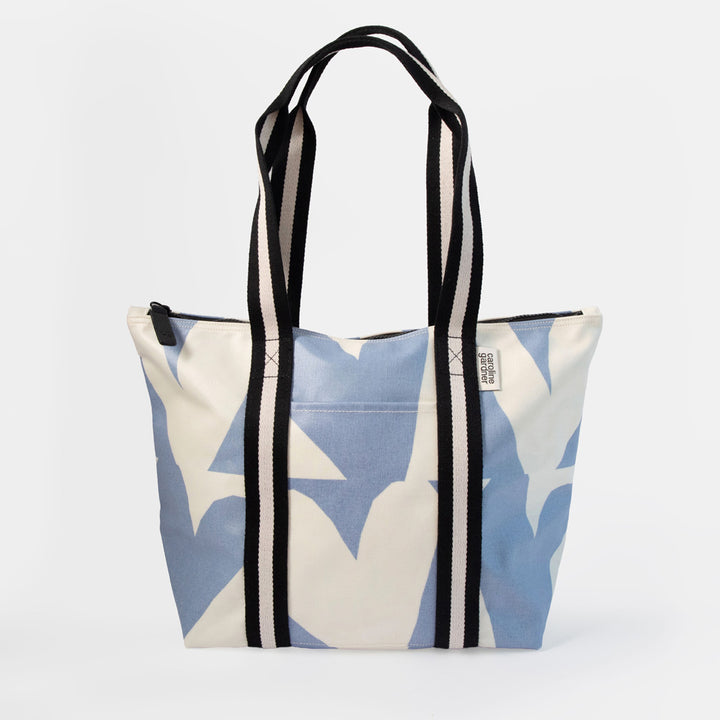 A canvas tote bag with a light blue and off-white star pattern, featuring black and white striped handles, shown against a plain light gray background.