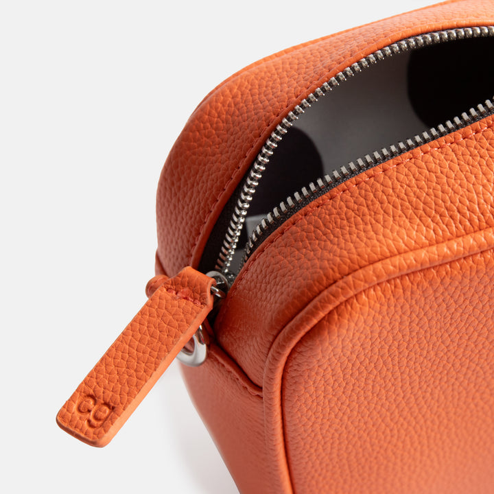 vegan leather orange camera bag with silver zip and hardware, monochrome webbing adjustable straps and spot print lining