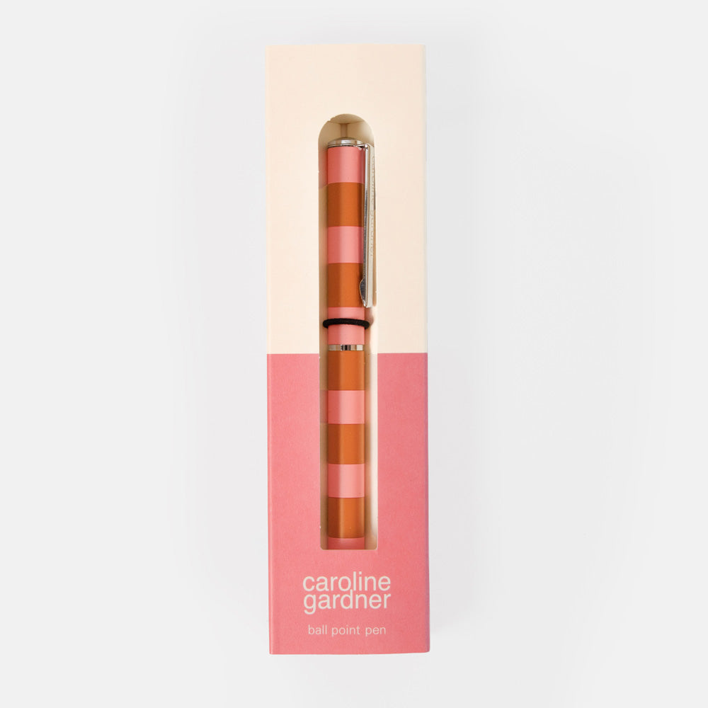 A Caroline Gardner ballpoint pen with a pink and orange striped pattern, presented inside its cream and pink packaging box against a light gray background.