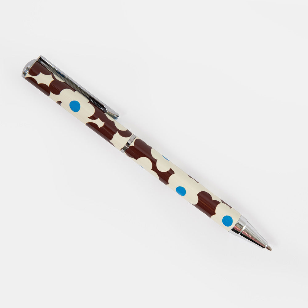 A ballpoint pen with a brown and cream flower print pattern, accented with small blue dots, shown on a plain light gray background.