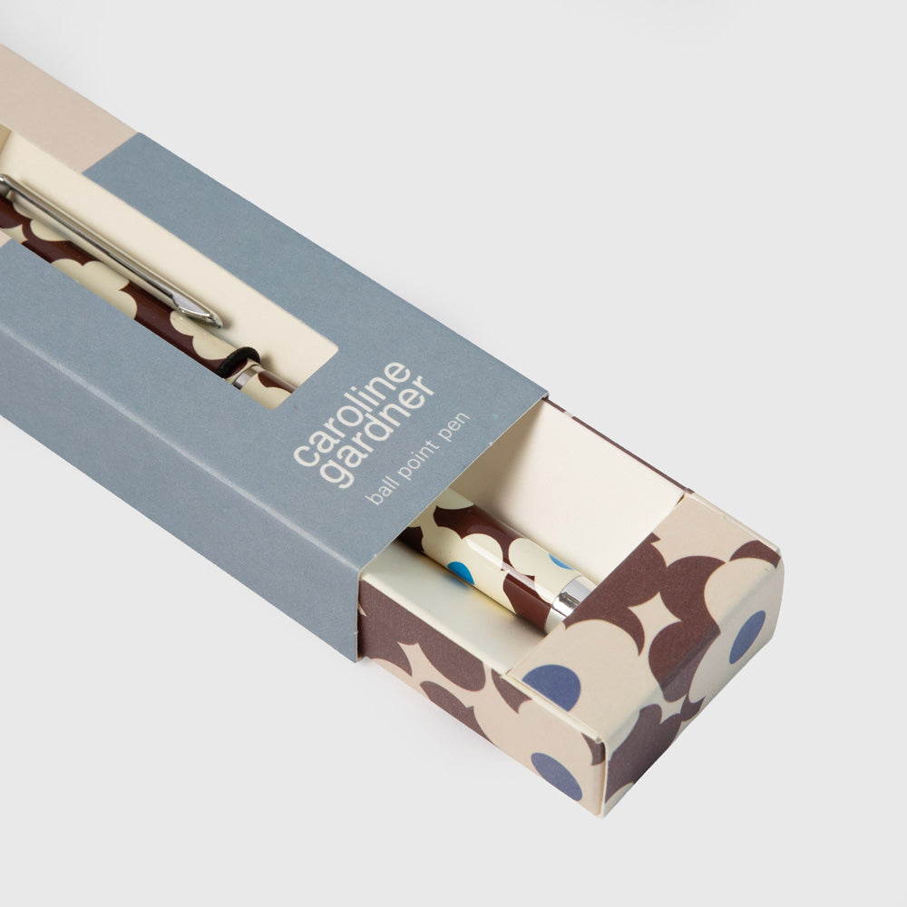 A Caroline Gardner ball point pen with a brown, cream, and blue floral pattern, presented in its original packaging box against a light gray background.