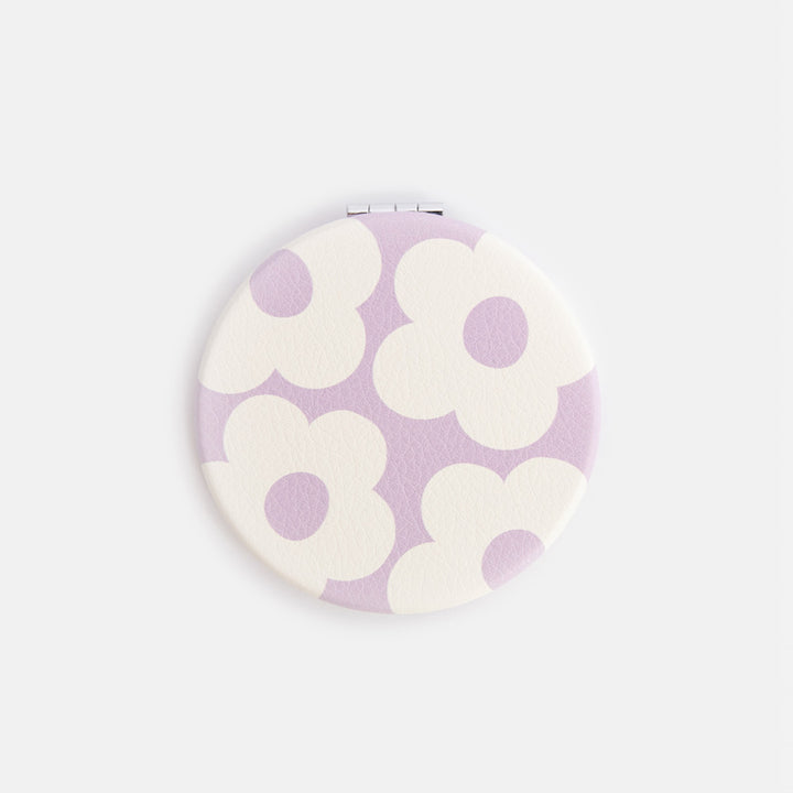 Round compact mirror with floral design on a light purple background
