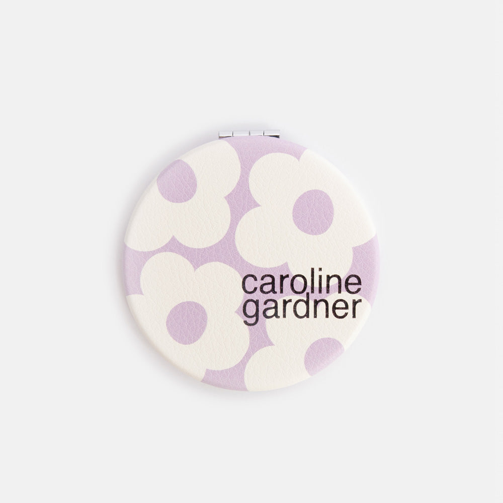 Round compact mirror with floral design and 'caroline gardner' branding on a white background