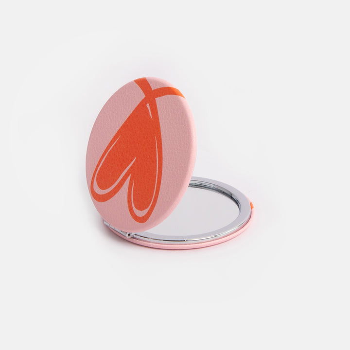 Compact mirror with a red heart design on a white background