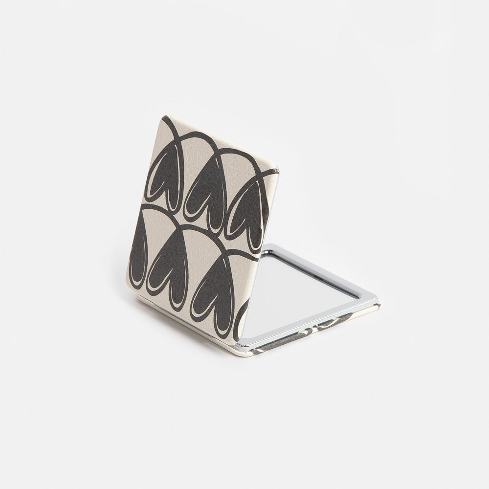 Compact mirror with black hearts print design on a white background