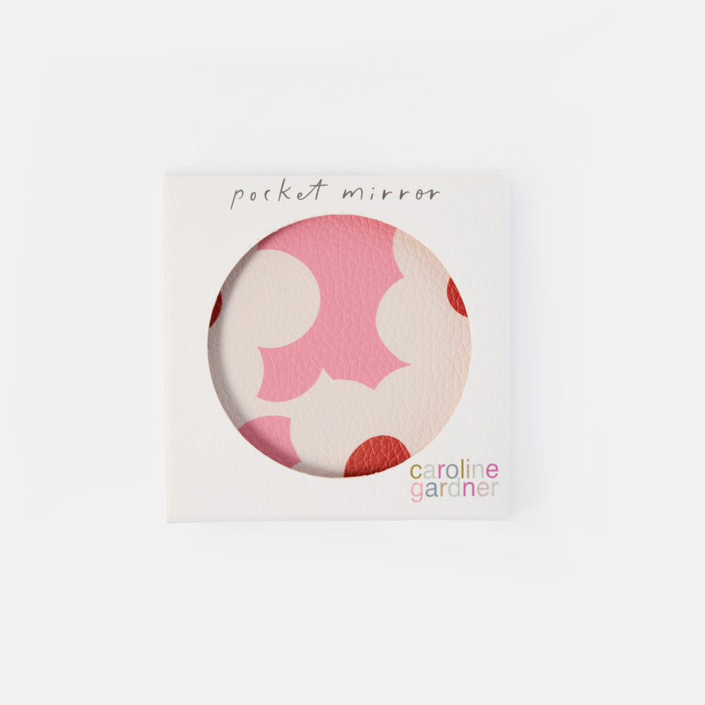 A square white packaging card for a pocket mirror by Caroline Gardner, featuring a circular cutout that reveals a pink and cream patterned mirror surface.
