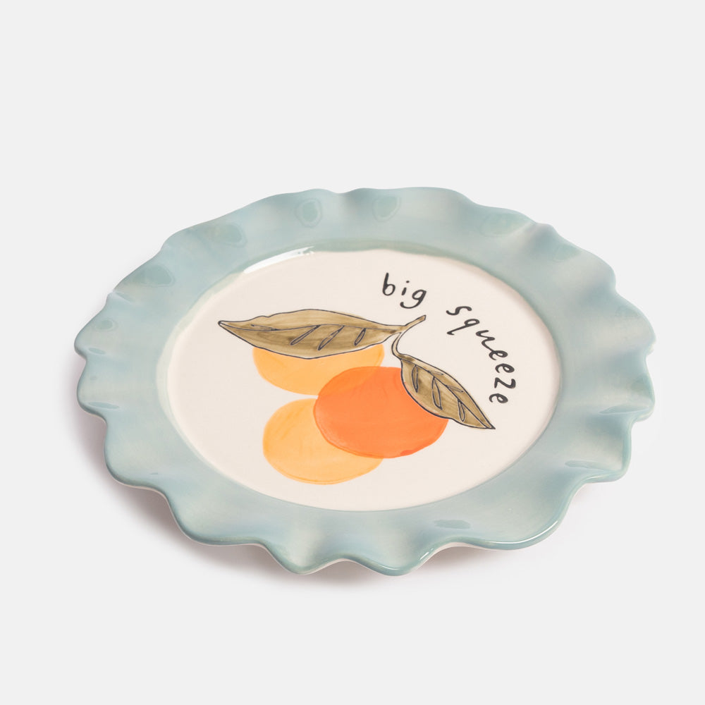 Ceramic plate with an illustration of 3 oranges with leave and 'big squeeze' text, finished with a light blue scalloped edge rim