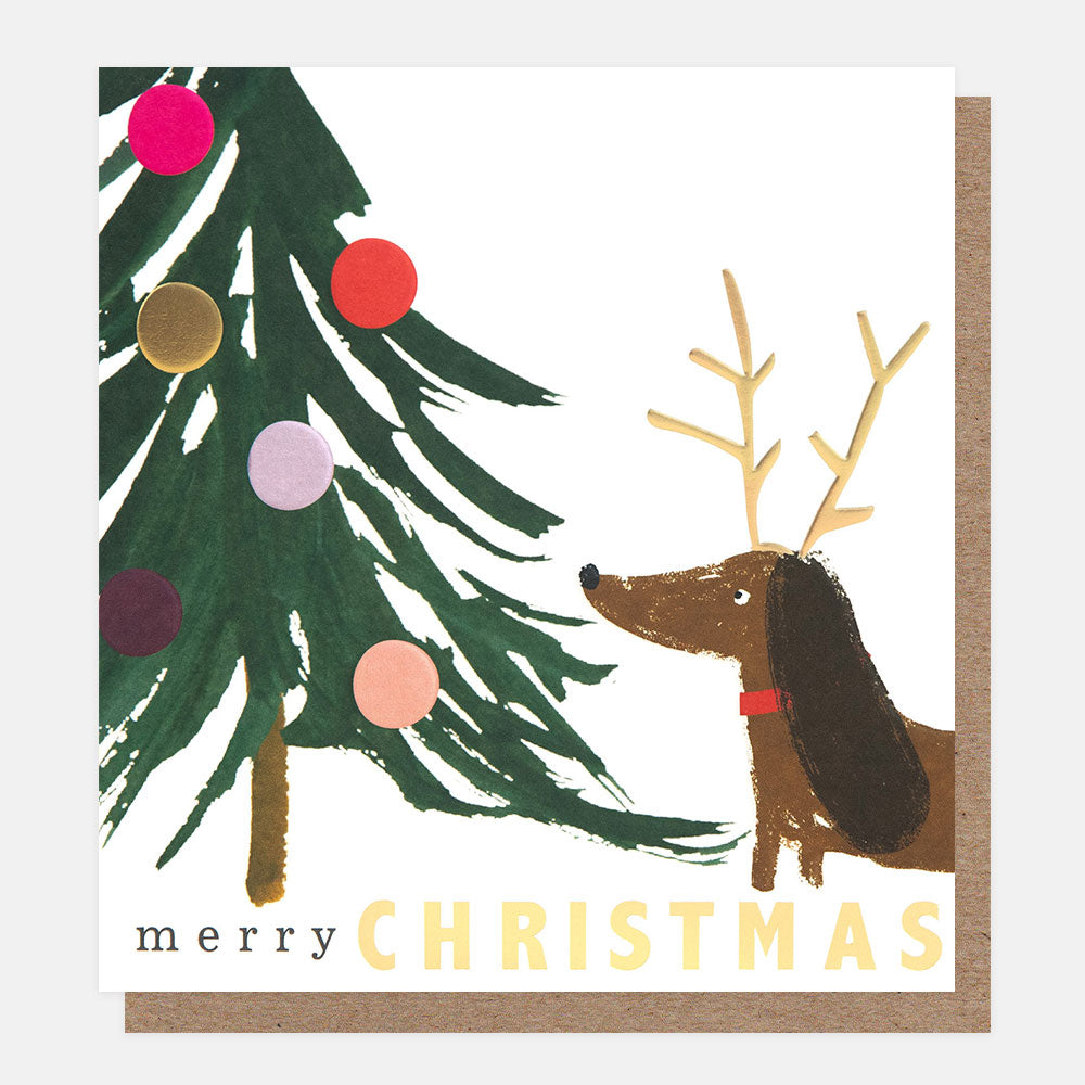 Christmas card with a dog wearing antlers and a decorated tree, featuring the text 'merry CHRISTMAS'.