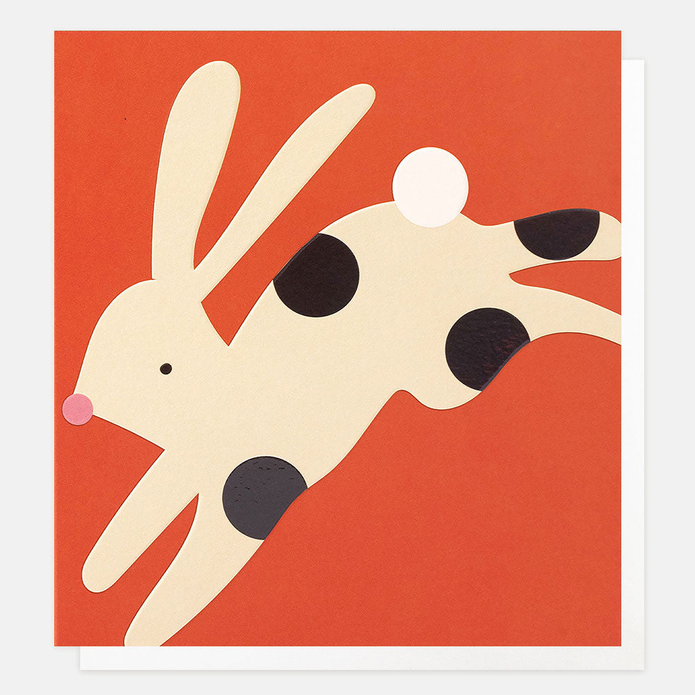 a greetings card with a stylised illustration of a cream rabbit with black spots against a bright orange background 