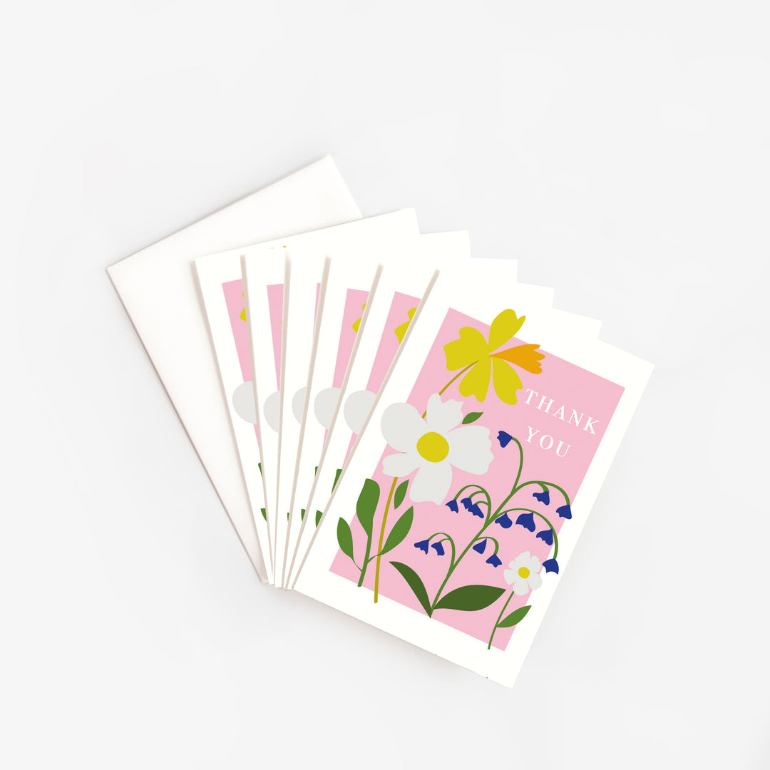 Six cards fanned out next to a white envelope, each with yellow, white and blue flowers on a pink panel and the words 'thank you' in white capital letters.