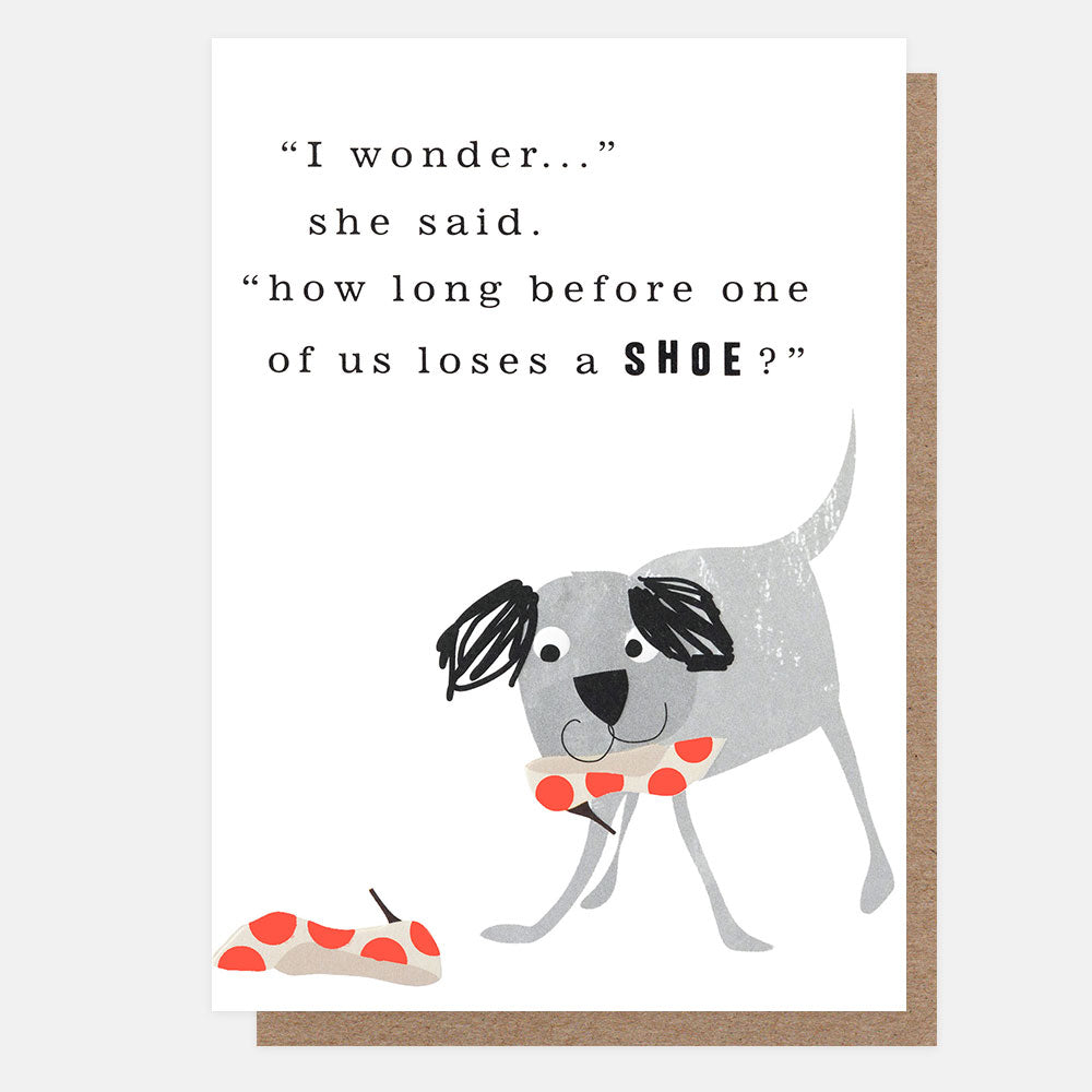 A square greeting card with a brown kraft envelope behind it. The card features an illustration of a grey dog with a colourful spotty high heel in its mouth and the text "i wonder..." she said. "how long before one of us loses a shoe?"