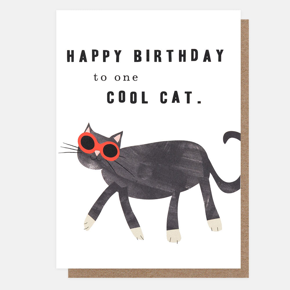 A birthday card with a white front and kraft brown envelope behind it. The card features an illustration of a grey cat wearing big red sunglasses and the text 'HAPPY BIRTHDAY to one COOL CAT.