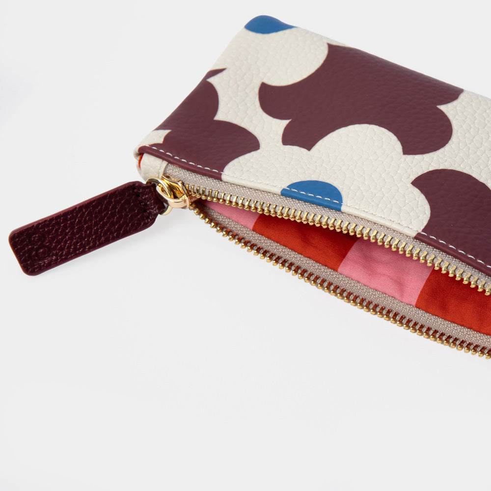 A close-up of a zippered pouch with a cream background and dark brown abstract cloud-like pattern, accented with small blue dots and a pink interior lining, shown on a light gray background.