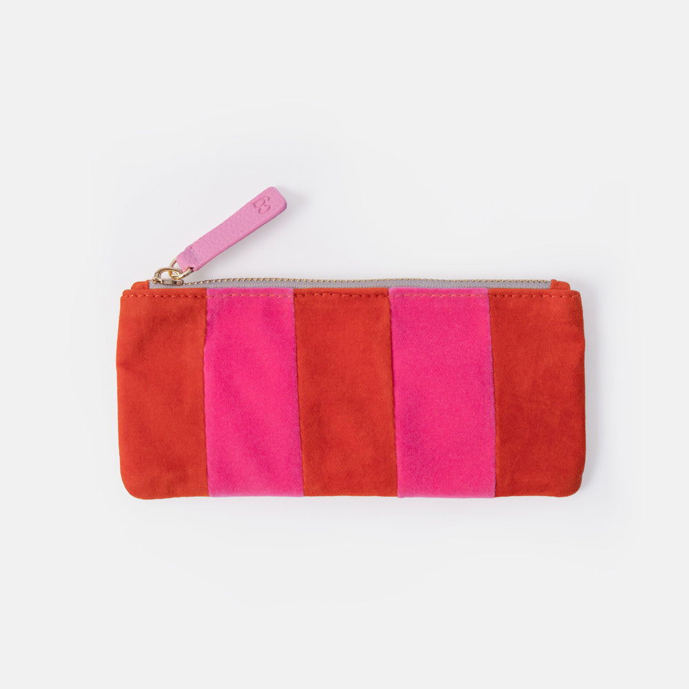 A rectangular zip pouch made of colourful velvet fabric panels in red, orange, and pink, with a light pink zipper pull, shown on a plain light gray background.