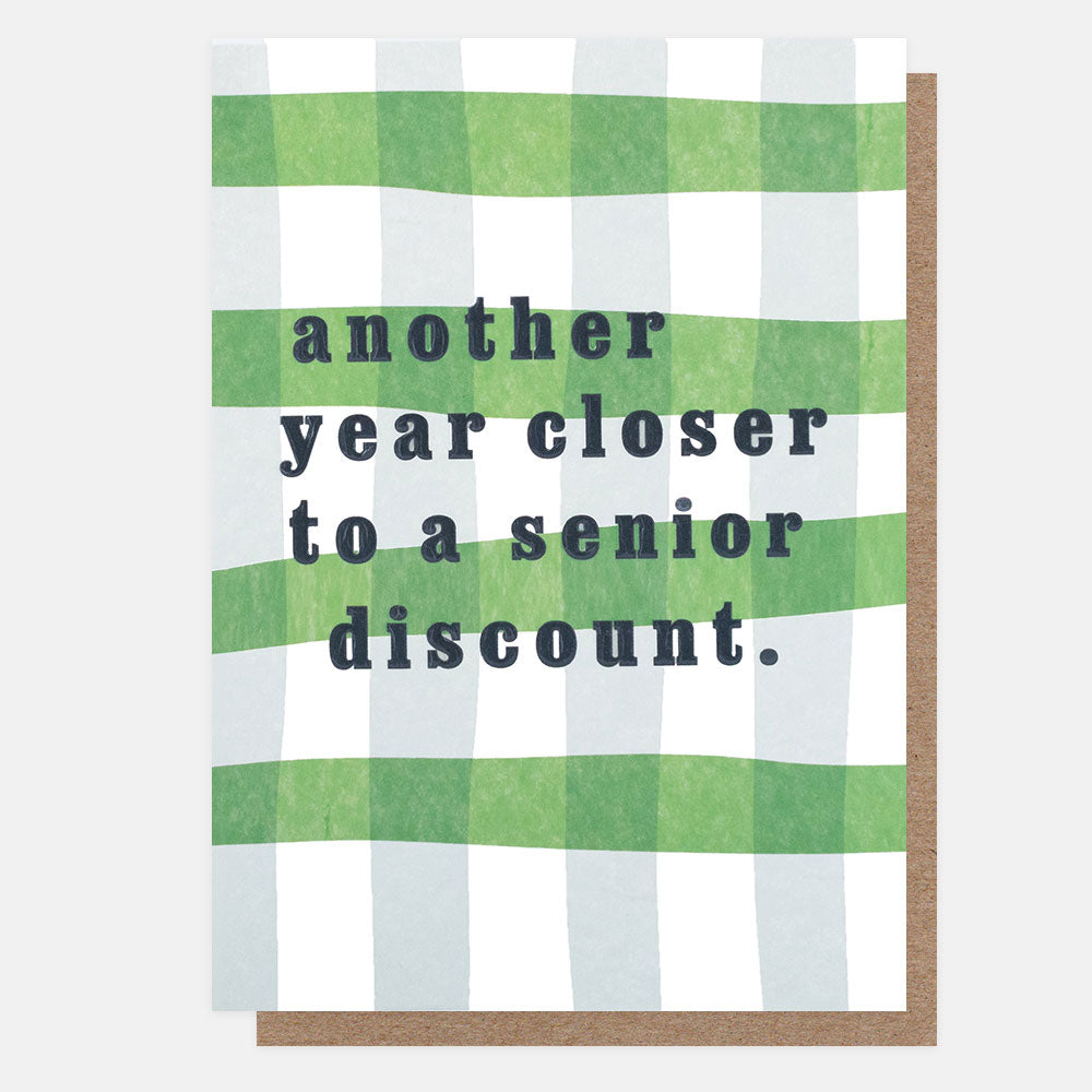 A greeting card with a green and white gingham pattern and the text 'another year closer to a senior discount.' in dark gray, shown with a brown envelope behind it on a light gray background.