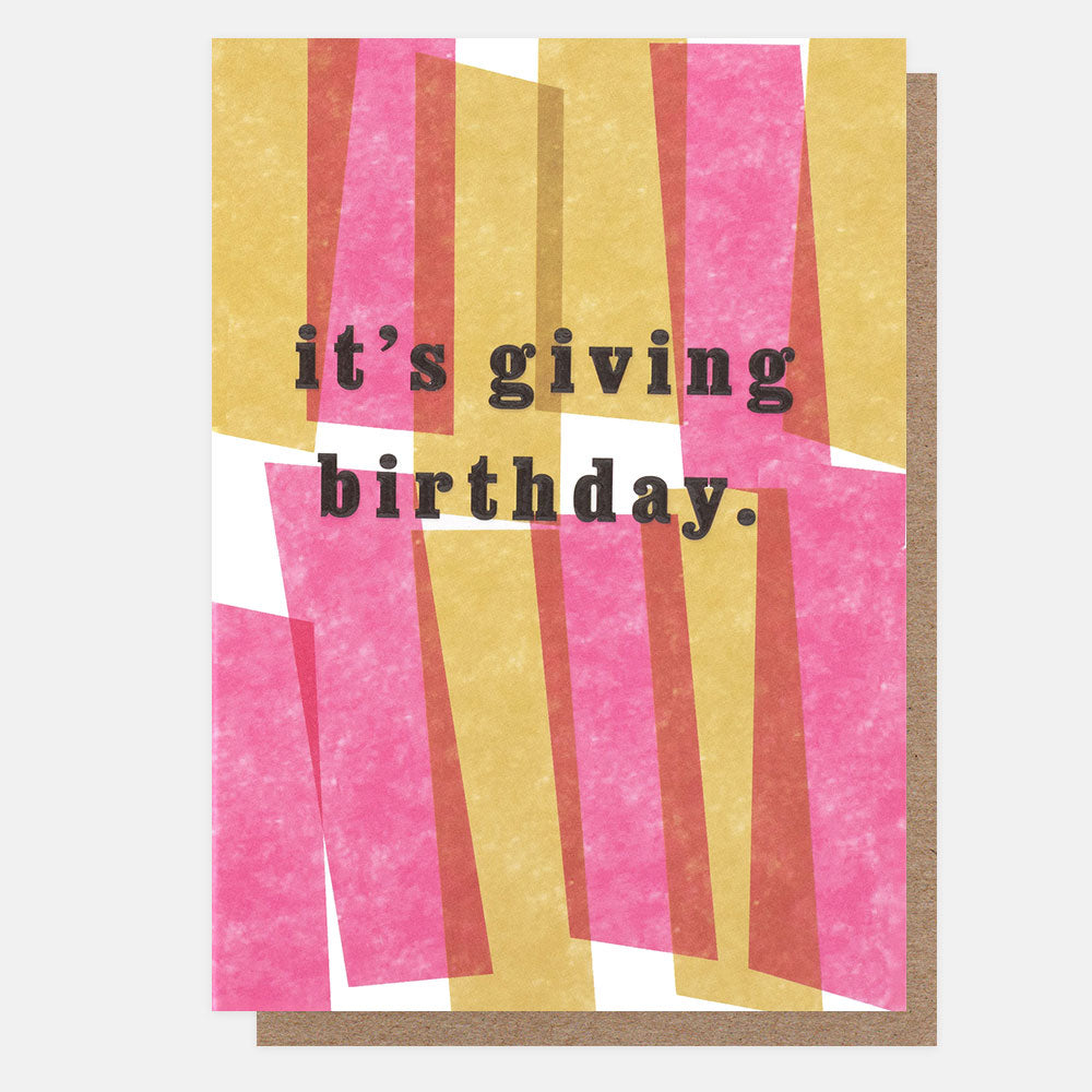 A greetings card with overlapping blocks of pink and mustard yellow and the text 'it's giving birthday.' in black embossed lettering, shown with a brown kraft envelope behind it.