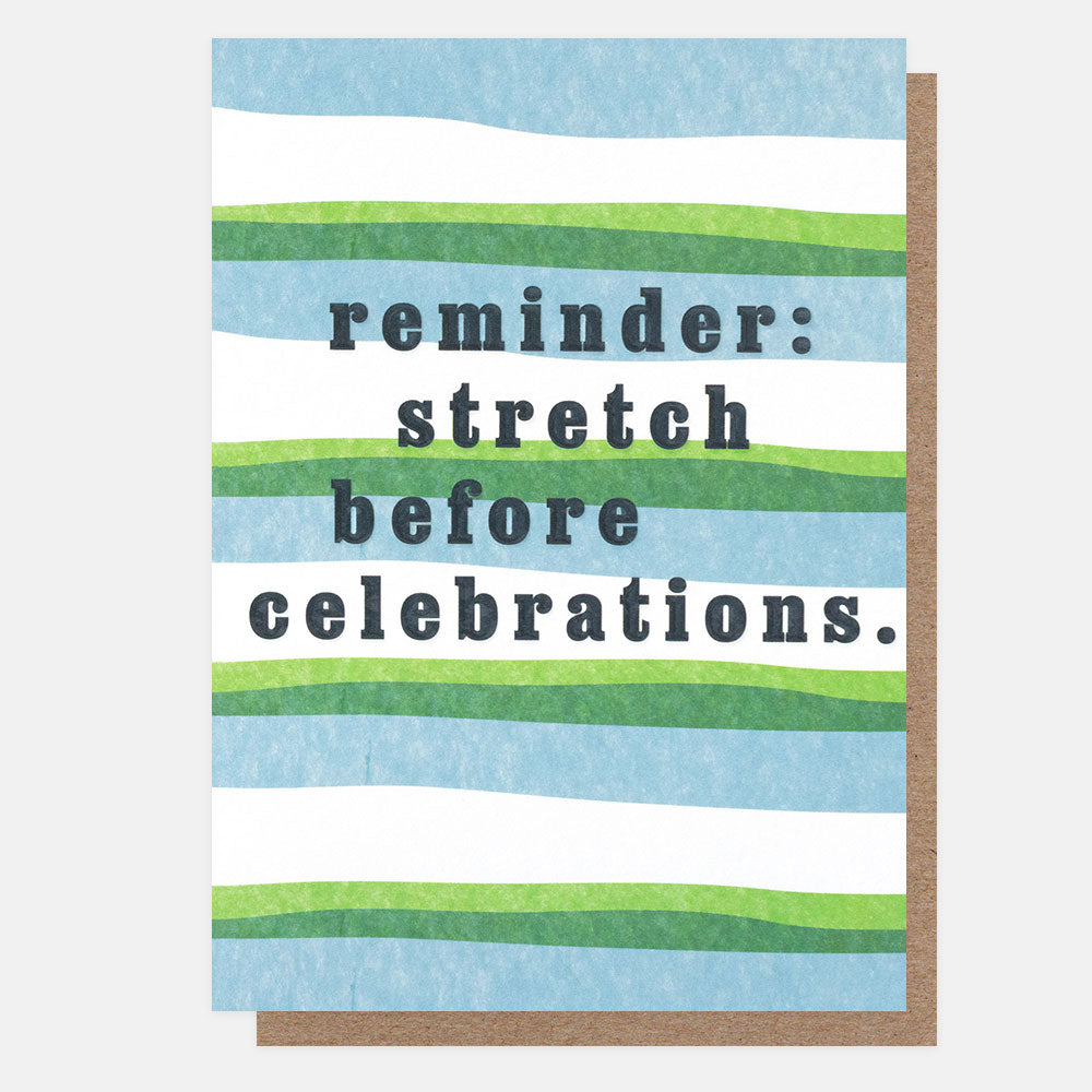 A greetings card with wavy blue, green and white horizontal stripes and the text 'reminder: stretch before celebrations.' in navy embossed lettering, shown with a brown kraft envelope behind it.