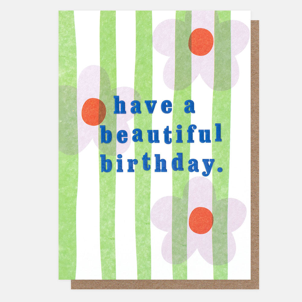 A greetings card with lilac flowers with orange centres on green and white vertical stripes and the text 'have a beautiful birthday.' in blue embossed lettering, shown with a brown kraft envelope behind it.