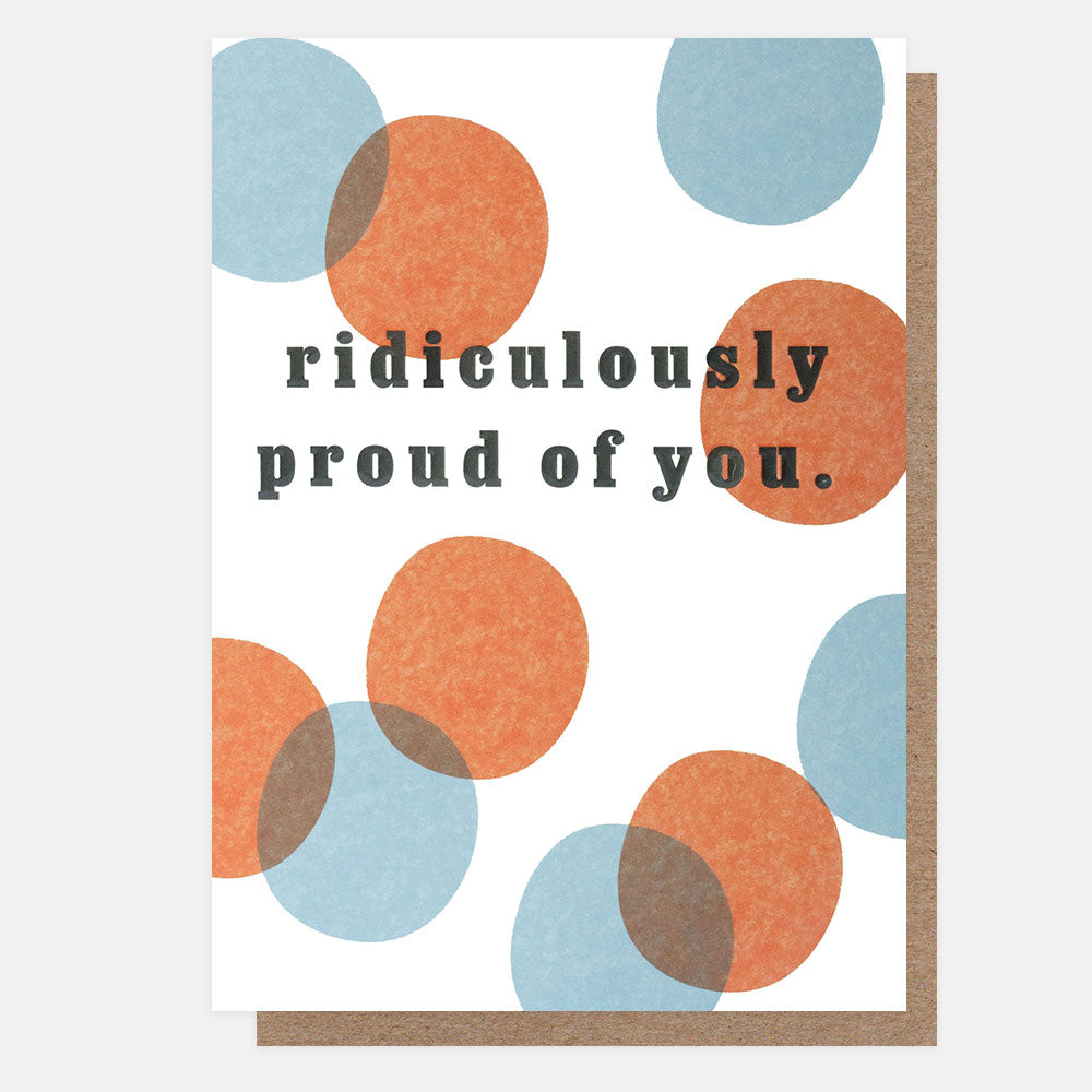 A greetings card with overlapping orange and blue spots on a white background and the text 'ridiculously proud of you.' in black embossed lettering, shown with a brown kraft envelope behind it.
