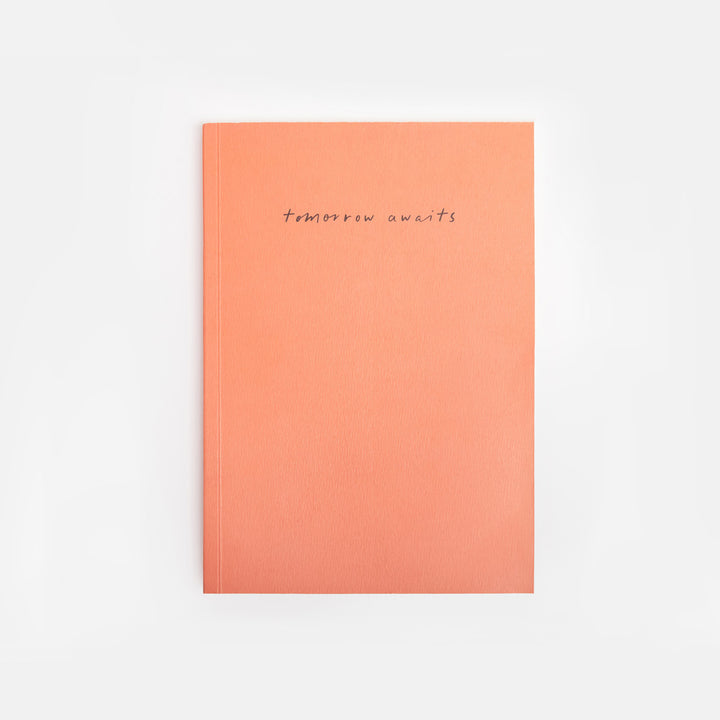 orange notebook with 'tomorrow awaits' text on a white background