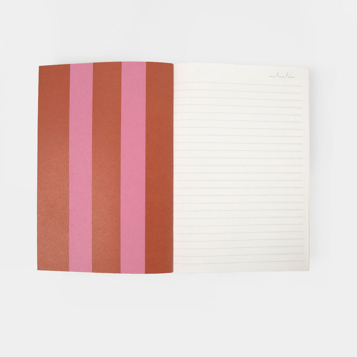 An open lined notebook with a striped cover in terracotta, dark brown, and pink, photographed on a clean white background.