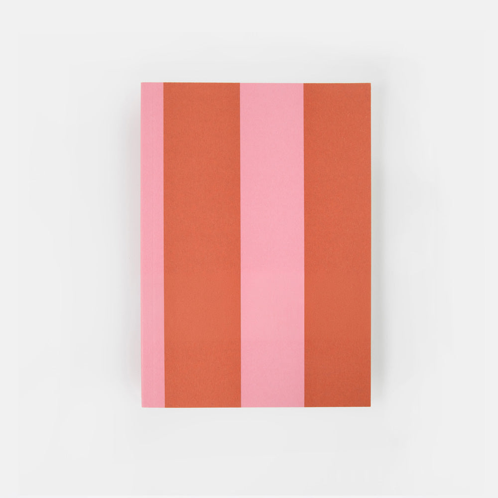 A notebook or journal with a minimalist cover design featuring vertical stripes in terracotta orange, light pink, and coral pink, with the text 'caroline garonier' printed in black near the bottom. The item is photographed flat against a clean, light gray background.