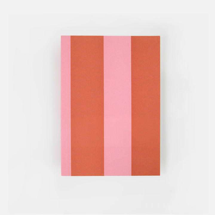 A notebook or journal with a minimalist cover design featuring vertical stripes in terracotta orange, light pink, and coral pink, with the text 'caroline garonier' printed in black near the bottom. The item is photographed flat against a clean, light gray background.