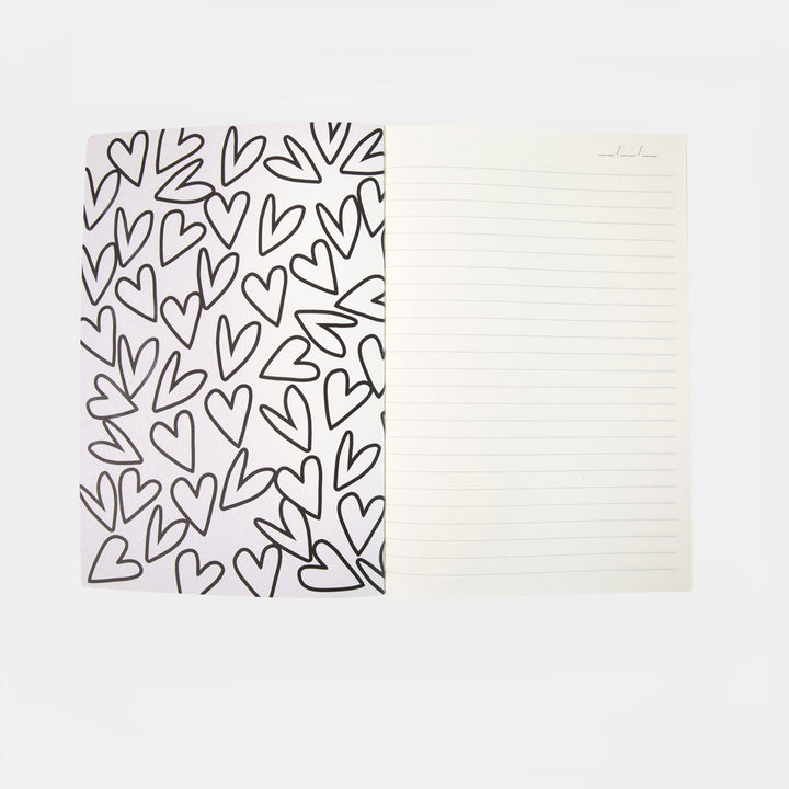 A lined notepad with a white cover decorated with a black hand-drawn heart pattern, shown open on a light gray background.