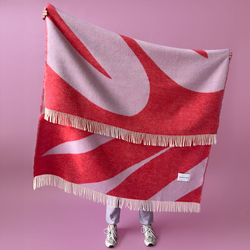 Person holding up a red and lilac squiggle stripe pure wool blanket, woven in Europe and made by Maison Deux