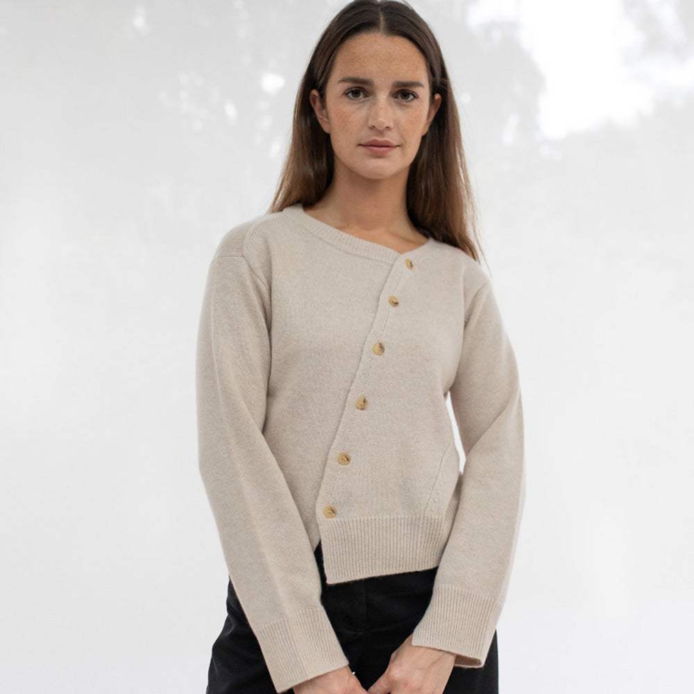 Woman wearing a beige asymmetrical cardigan with buttons 