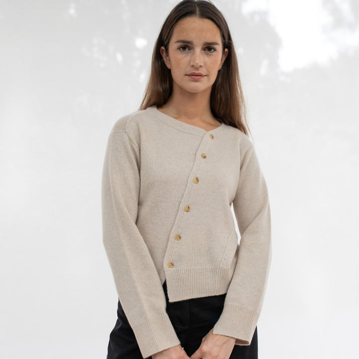 Woman wearing a beige asymmetrical cardigan with buttons 