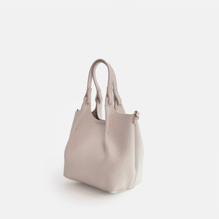 white leather tote style handbag with a spare matching strap on a white background