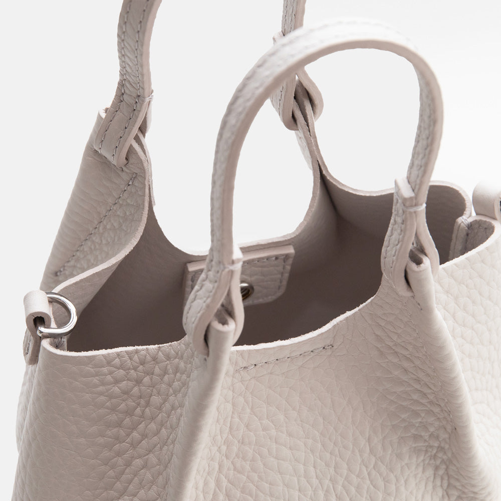 white leather tote style handbag with a spare matching strap on a white background