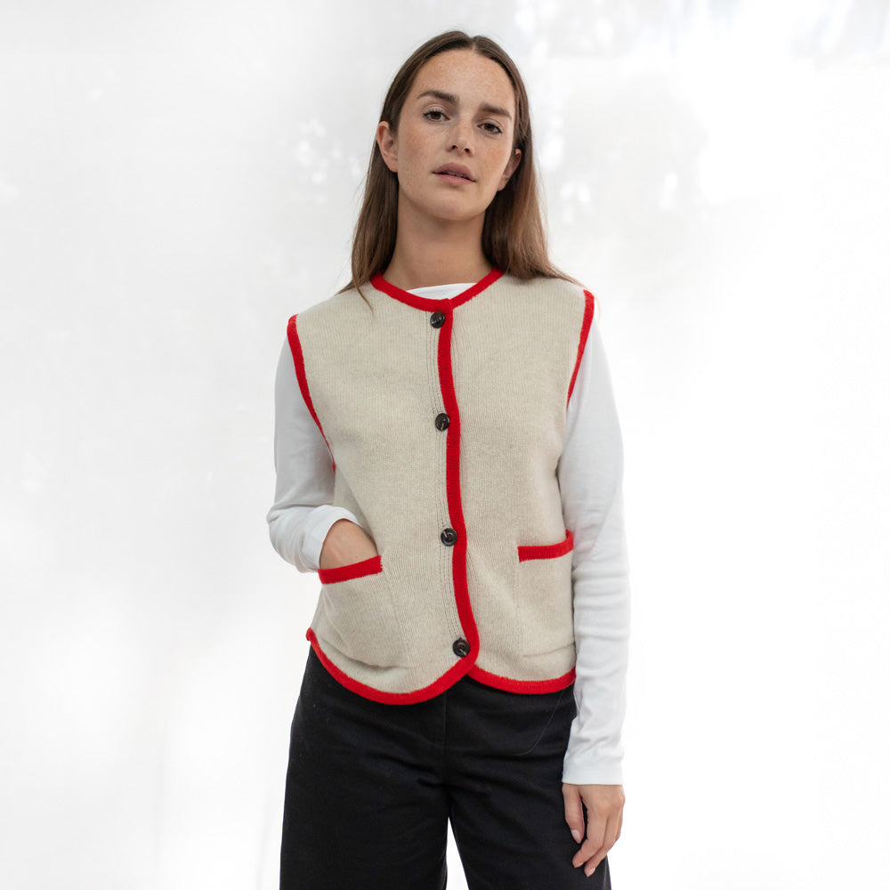 Woman wearing a beige vest with red trim on a white background