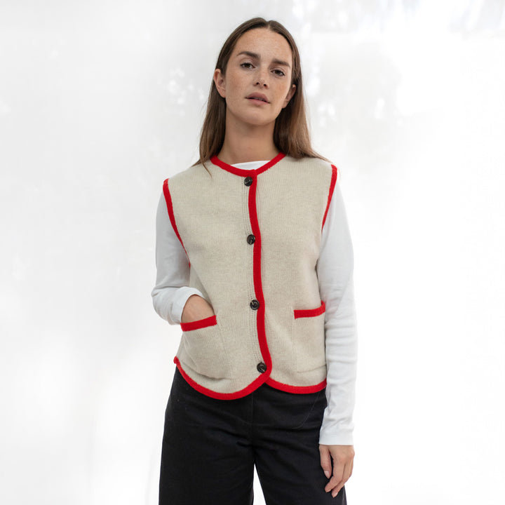 Woman wearing a beige vest with red trim on a white background