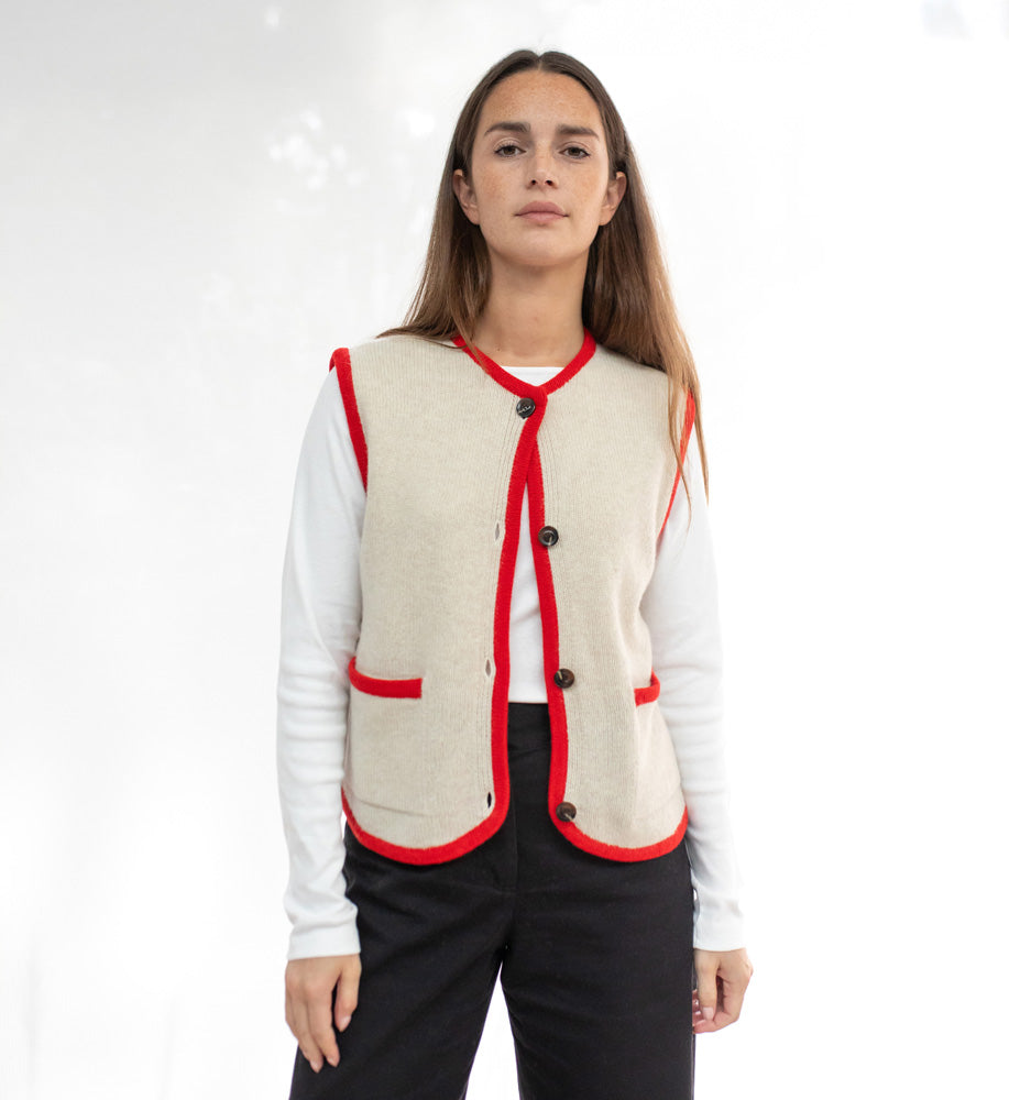 Woman wearing a beige vest with red trim on a white background