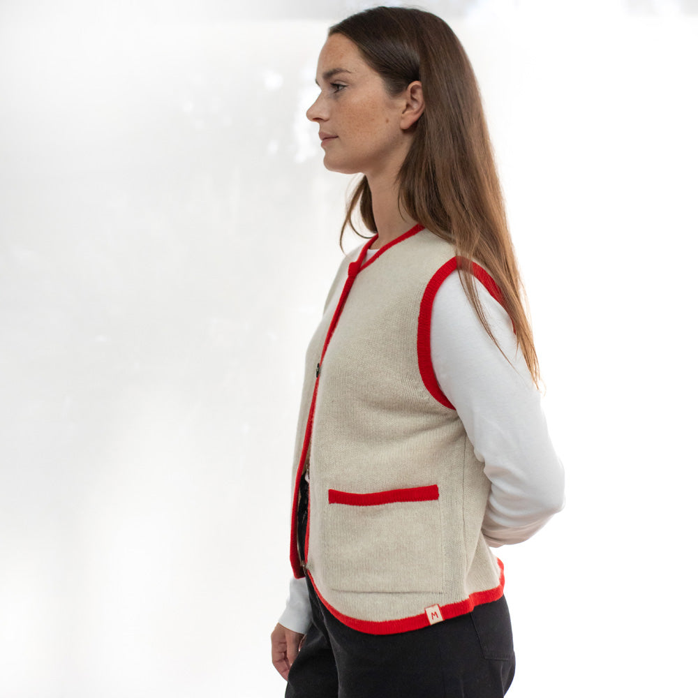 Woman wearing a beige vest with red accents on a white background