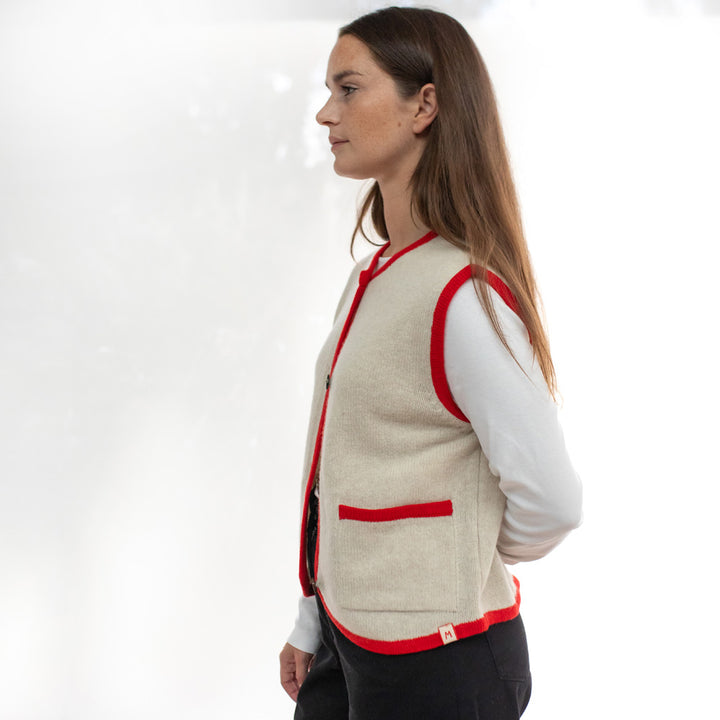Woman wearing a beige vest with red accents on a white background
