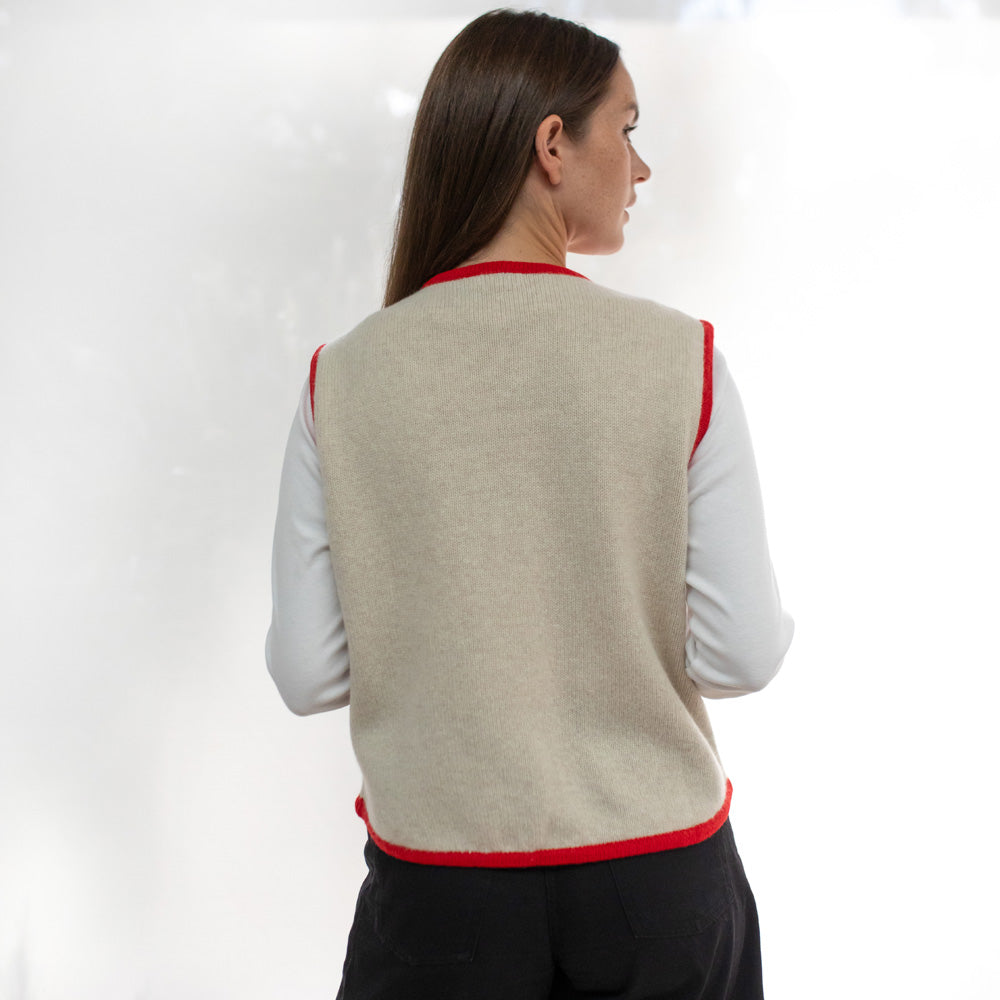 Woman wearing a beige vest with red trim on a white background