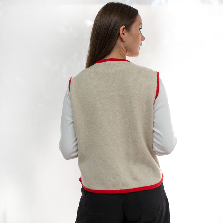 Woman wearing a beige vest with red trim on a white background