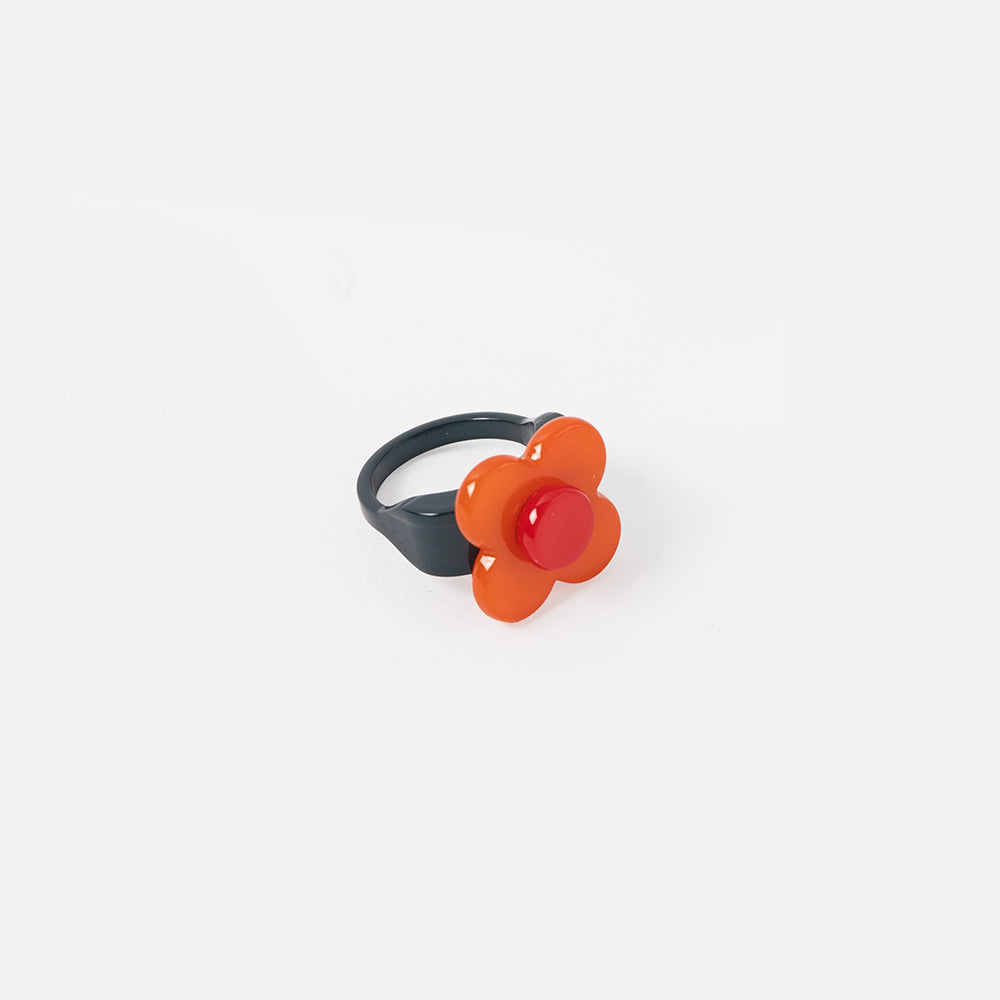Flower-shaped ring with orange center and black band on a white background
