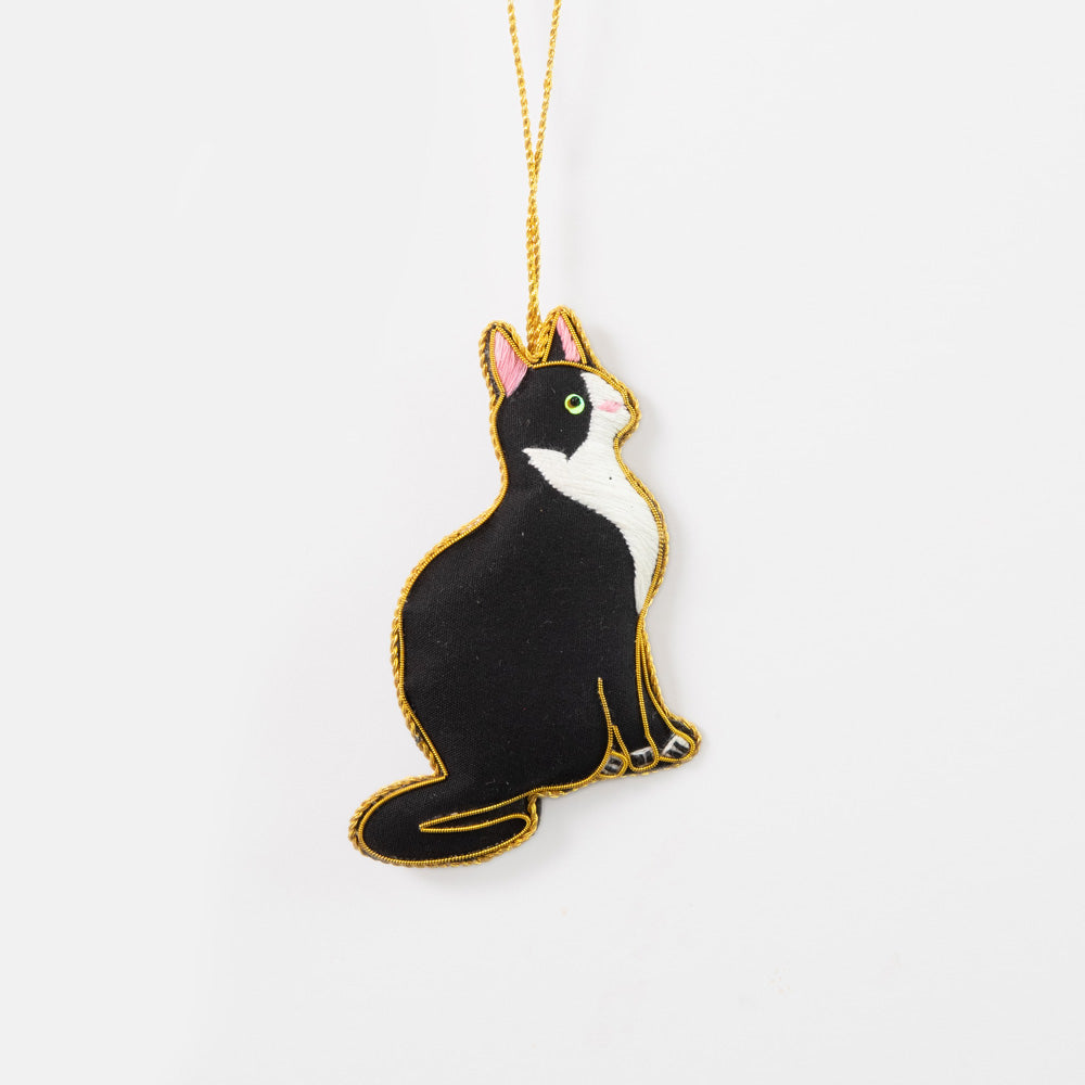 Cat-shaped hanging christmas tree decoration with black and white design on a gold chain against a white background