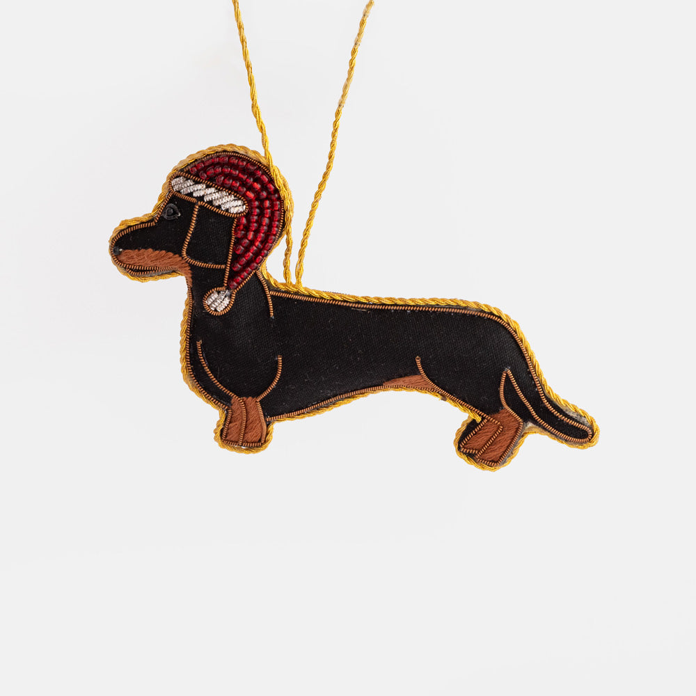 Beaded sausage dog Christmas tree decoration in black and tan with a red beaded Santa hat, hanging from a gold cord