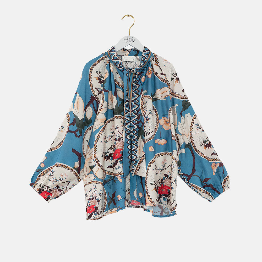 women's tie neck pussy bow shirt blouse featuring print of decorative floral plates and white magnolia on a bright blue base