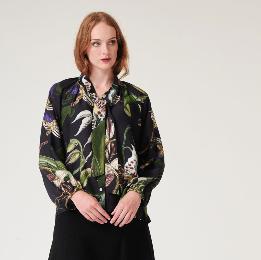 black pussy bow blouse shirt with orchid print in green, blue, ivory and yellow, worn with a black a line skirt